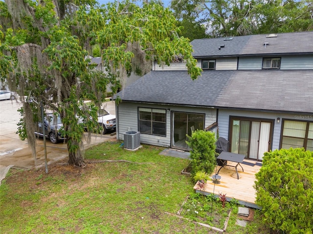 back of house with a wooden deck, a shingled roof, a lawn, and central AC unit