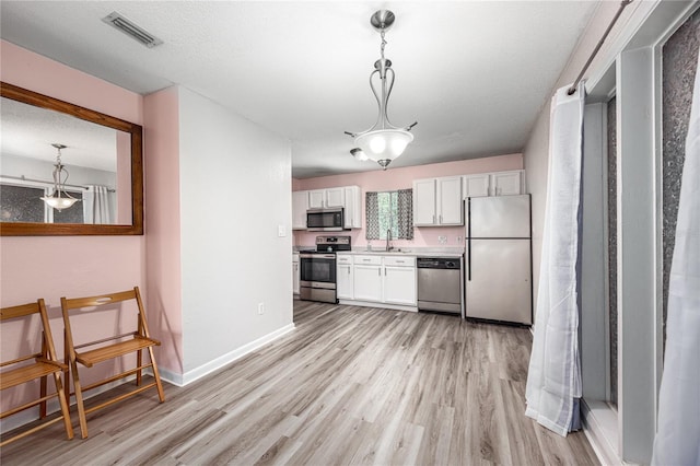 507 NW 39th Rd Unit 235, Gainesville, FL 32607 - kitchen featuring appliances with stainless steel finishes, light wood-style floors, white cabinets, and hanging light fixtures