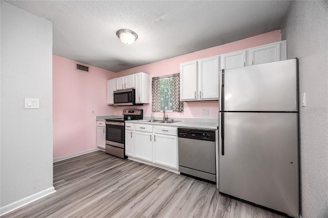 507 NW 39th Rd Unit 235, Gainesville, FL 32607 - kitchen featuring appliances with stainless steel finishes, white cabinets, light wood-style flooring, and a textured ceiling