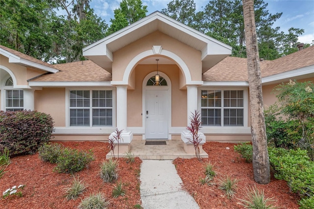 entrance to property featuring a shingled roof and stucco siding