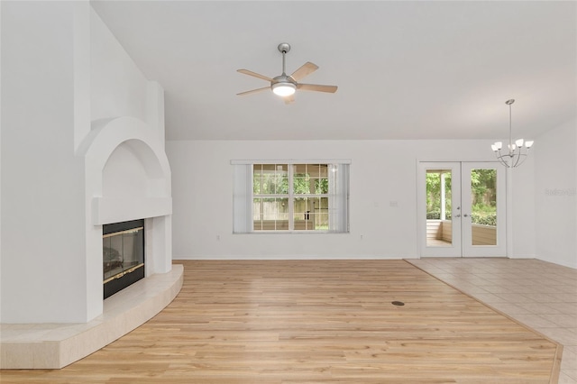 unfurnished living room with french doors, a ceiling fan, a fireplace, vaulted ceiling, and a chandelier