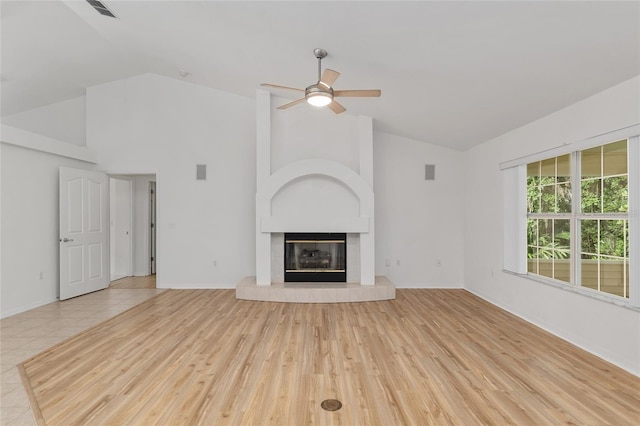unfurnished living room with a ceiling fan, a tiled fireplace, baseboards, wood finished floors, and high vaulted ceiling