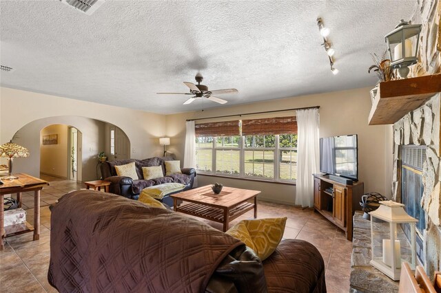 7450 SE State Road 121, Morriston, FL 32668 - living room with arched walkways, light tile patterned floors, ceiling fan, a textured ceiling, and a stone fireplace