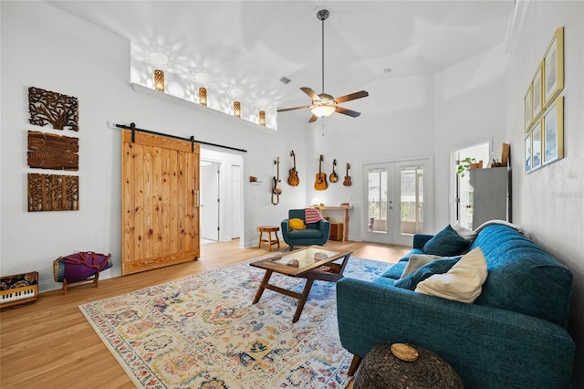living room featuring french doors, wood finished floors, ceiling fan, a towering ceiling, and a barn door