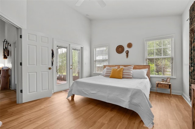 bedroom with access to exterior, multiple windows, light wood-style floors, ceiling fan, and a towering ceiling