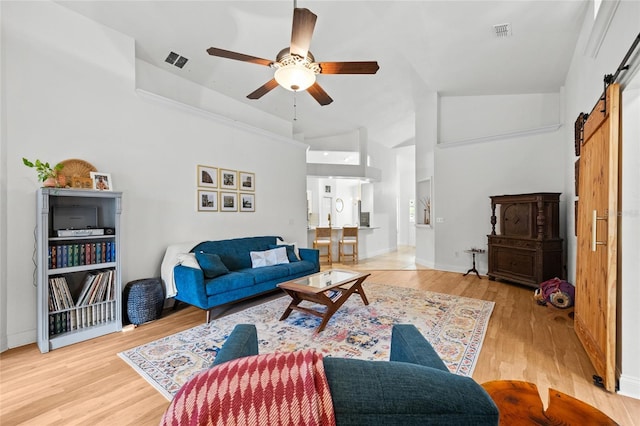 living area with a barn door, a ceiling fan, light wood-type flooring, and baseboards