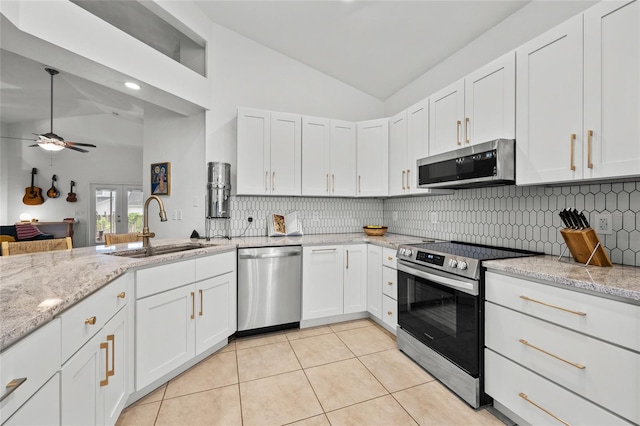 kitchen with appliances with stainless steel finishes, a sink, light tile patterned floors, decorative backsplash, and high vaulted ceiling