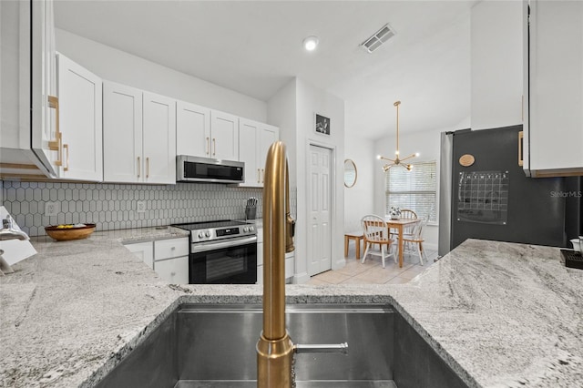 kitchen featuring stainless steel appliances, decorative backsplash, white cabinets, light stone counters, and a chandelier