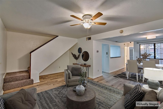living area featuring stairs, wood finished floors, ceiling fan, and baseboards