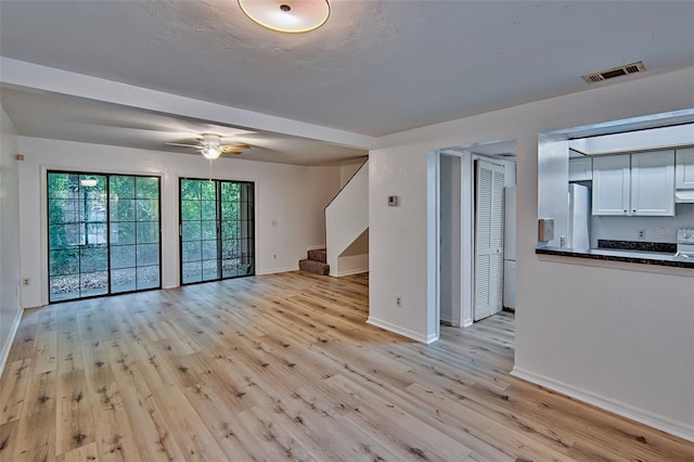 unfurnished living room with stairway, light wood-style floors, baseboards, and ceiling fan