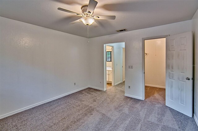 unfurnished bedroom with a spacious closet, carpet, baseboards, ceiling fan, and ensuite bath