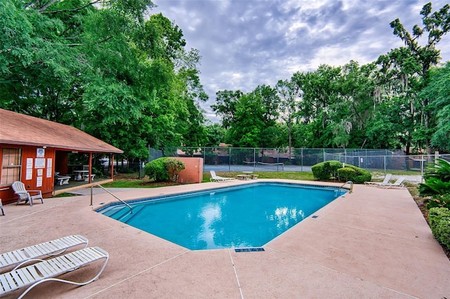 community pool with a patio area, view of scattered trees, and fence