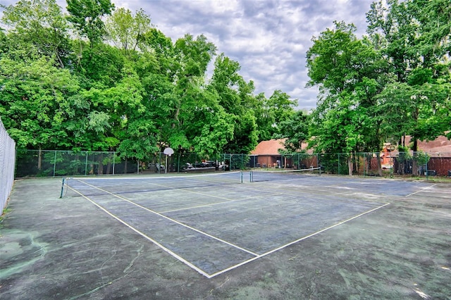 view of tennis court with fence and view of wooded area