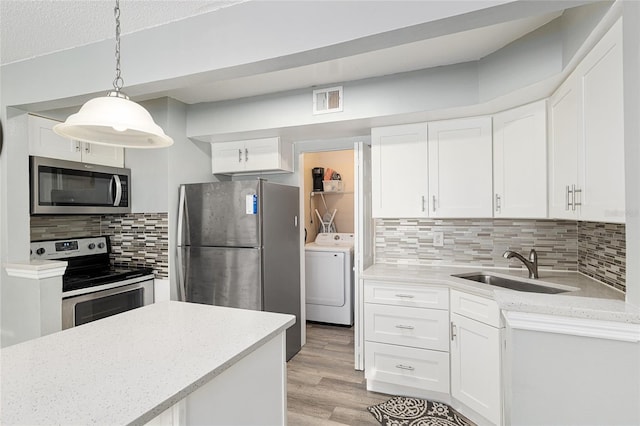 2601 SW Archer Rd Unit G 128, Gainesville, FL 32608 - kitchen featuring appliances with stainless steel finishes, washer / clothes dryer, a sink, light wood finished floors, and white cabinetry