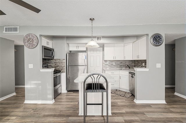2601 SW Archer Rd Unit G 128, Gainesville, FL 32608 - kitchen featuring appliances with stainless steel finishes, decorative backsplash, white cabinets, a textured ceiling, and dark wood-type flooring