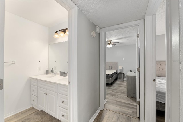 2601 SW Archer Rd Unit G 128, Gainesville, FL 32608 - ensuite bathroom featuring a textured ceiling, ceiling fan, wood finished floors, double vanity, and baseboards