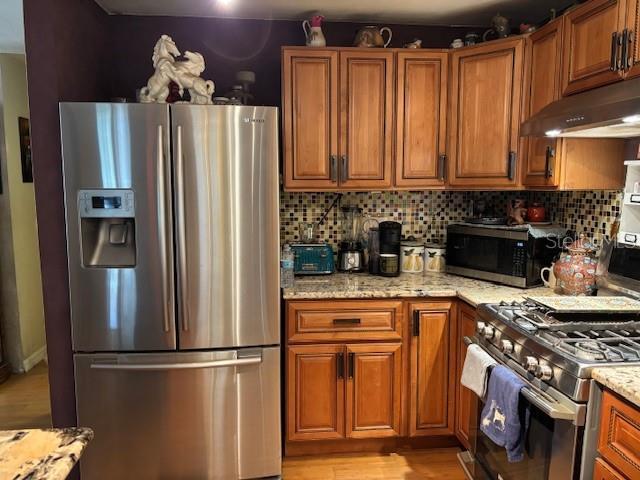 6410 SW 170th St, Archer, FL 32618 - kitchen with appliances with stainless steel finishes, under cabinet range hood, brown cabinetry, and light stone counters