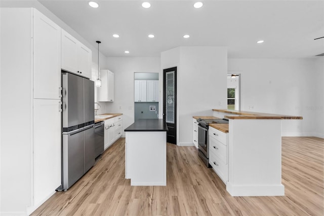 kitchen with appliances with stainless steel finishes, butcher block countertops, light wood-style flooring, a kitchen island, and white cabinets