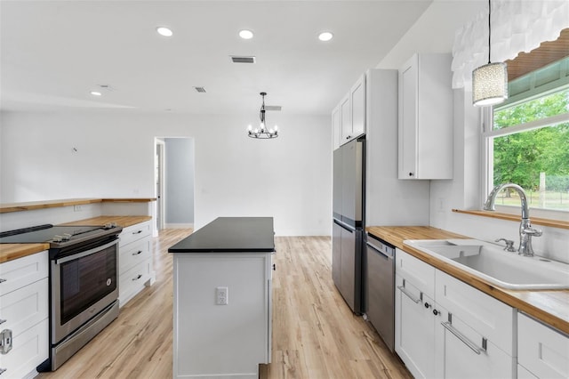 kitchen featuring stainless steel appliances, a sink, wooden counters, a center island, and recessed lighting