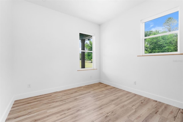 unfurnished room with healthy amount of natural light, wood finished floors, and baseboards