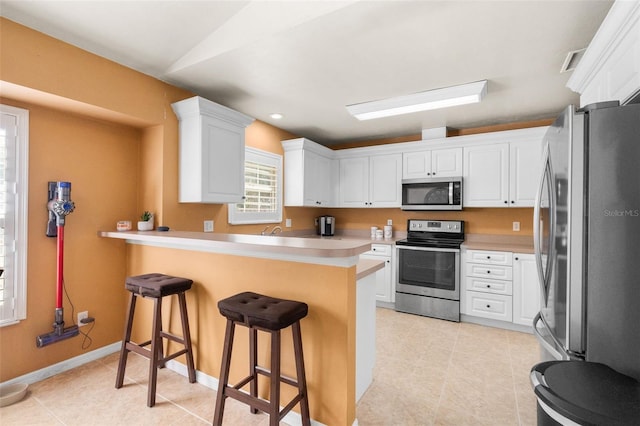1979 NW 86th Ter, Gainesville, FL 32606 - kitchen with appliances with stainless steel finishes, a peninsula, a breakfast bar area, white cabinetry, and light tile patterned floors