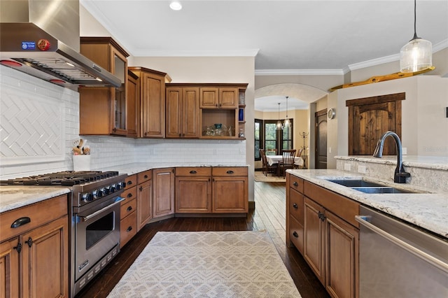 kitchen with stainless steel appliances, wall chimney range hood, a sink, dark wood finished floors, and arched walkways