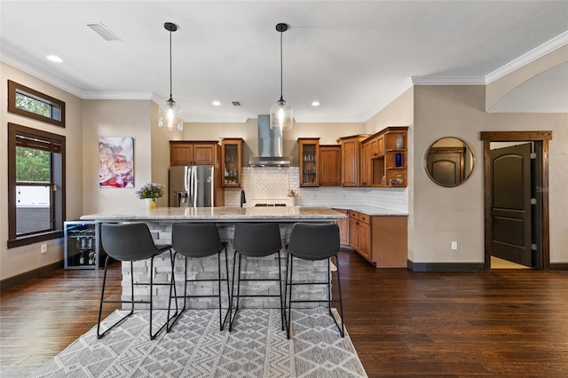 kitchen featuring stainless steel fridge, wall chimney range hood, brown cabinets, a breakfast bar, and open shelves