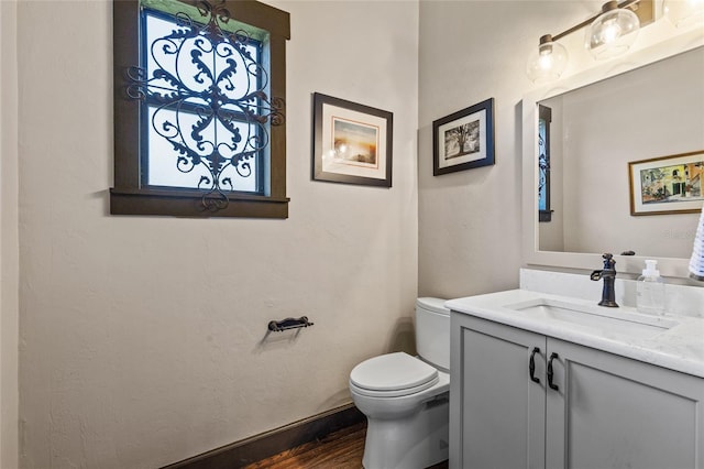 half bath featuring wood finished floors, toilet, vanity, and baseboards