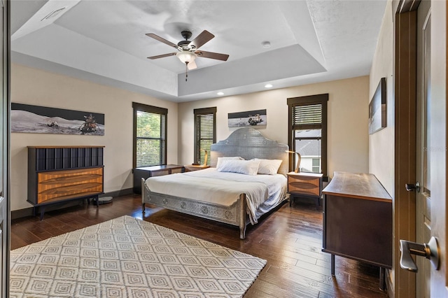 bedroom with a raised ceiling, dark wood-style flooring, baseboards, a ceiling fan, and recessed lighting