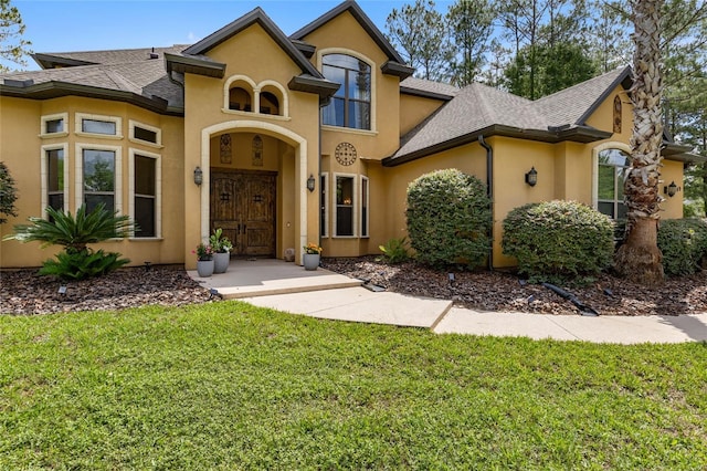 view of front facade featuring a front lawn, stucco siding, and a shingled roof