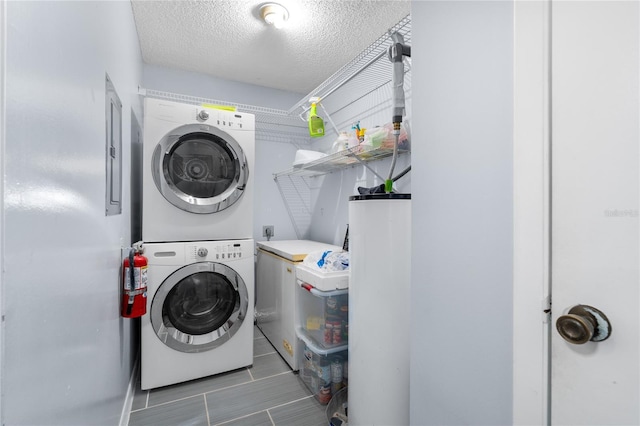 clothes washing area featuring water heater, estacked washer and dryer, and a textured ceiling