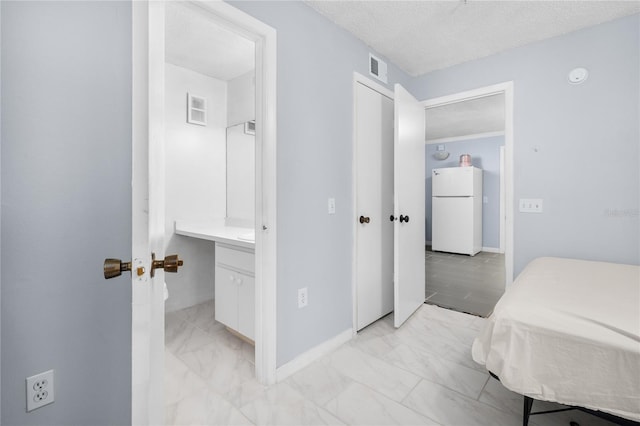 bedroom with freestanding refrigerator, light marble finish floors, baseboards, and a textured ceiling