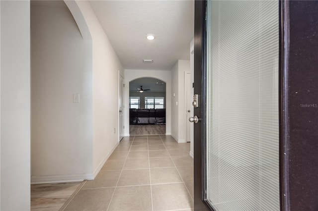 hallway featuring arched walkways, light tile patterned floors, and baseboards
