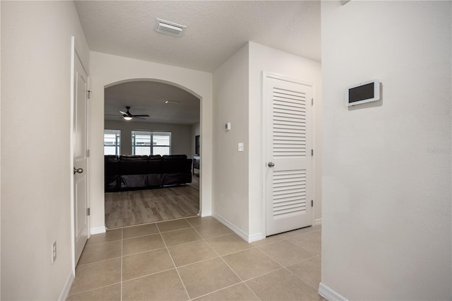 hallway featuring arched walkways, light tile patterned flooring, baseboards, and a textured ceiling