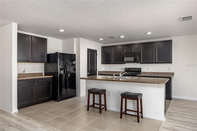 kitchen featuring black appliances, a sink, a breakfast bar area, a textured ceiling, and a center island with sink