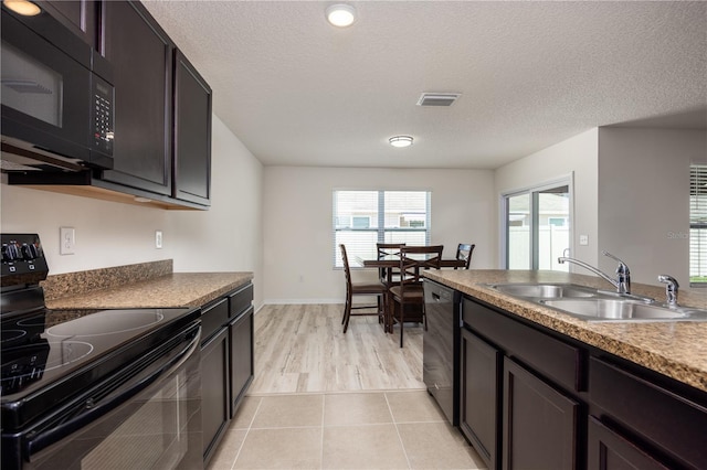 kitchen with black appliances, a sink, a textured ceiling, light tile patterned floors, and baseboards