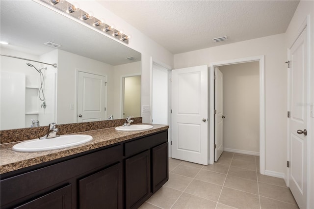 full bathroom featuring double vanity, tile patterned flooring, baseboards, and a textured ceiling