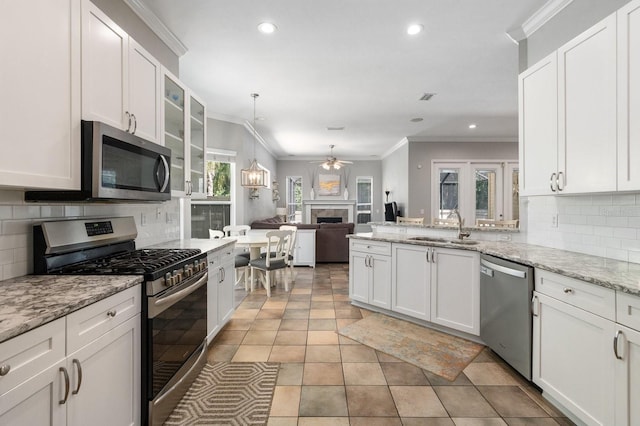 kitchen with stainless steel appliances, a sink, a ceiling fan, a tiled fireplace, and decorative backsplash