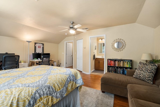 bedroom featuring lofted ceiling, an office area, wood finished floors, ensuite bath, and a ceiling fan