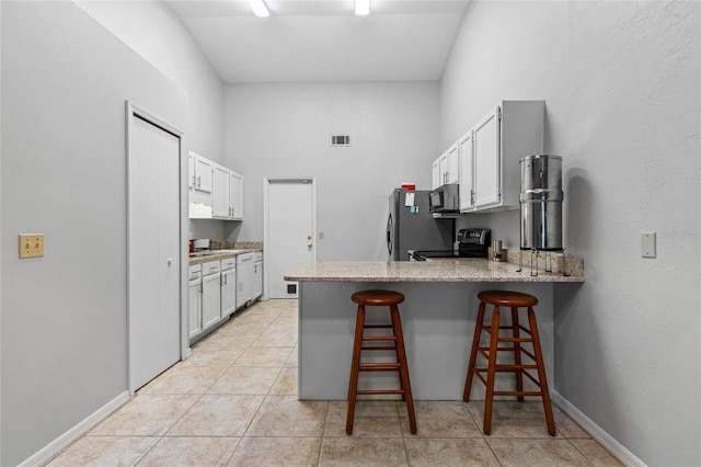 kitchen with stainless steel appliances, a peninsula, a kitchen bar, light stone counters, and baseboards