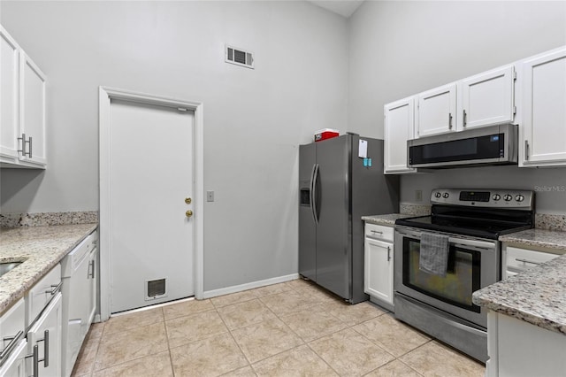 kitchen featuring stainless steel appliances, white cabinets, light stone counters, light tile patterned floors, and a towering ceiling
