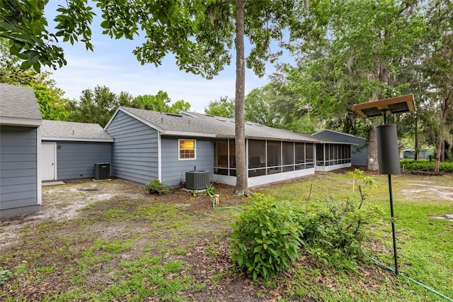 back of property with a sunroom, cooling unit, roof with shingles, and a lawn