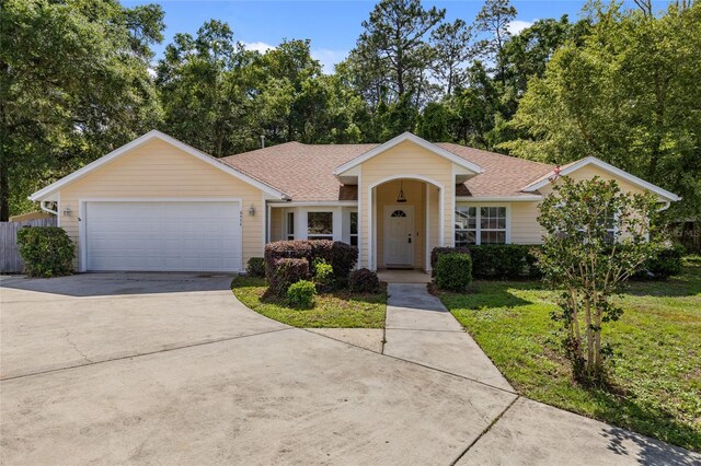 view of front facade with driveway, a garage, roof with shingles, a front lawn, and view of wooded area
