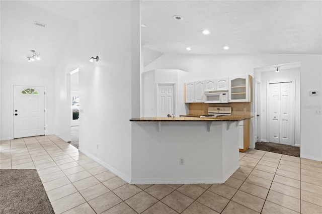 kitchen with white appliances, light tile patterned floors, a kitchen breakfast bar, white cabinets, and glass insert cabinets