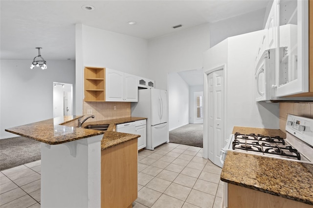 kitchen with a sink, white appliances, a peninsula, light tile patterned floors, and light carpet