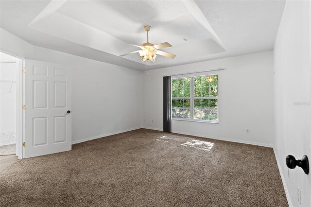 spare room featuring a raised ceiling, carpet flooring, baseboards, and a ceiling fan