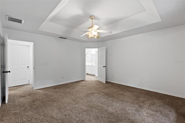 unfurnished bedroom featuring carpet flooring, a raised ceiling, baseboards, and a ceiling fan