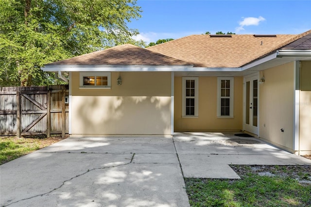 back of property with roof with shingles, fence, and a patio