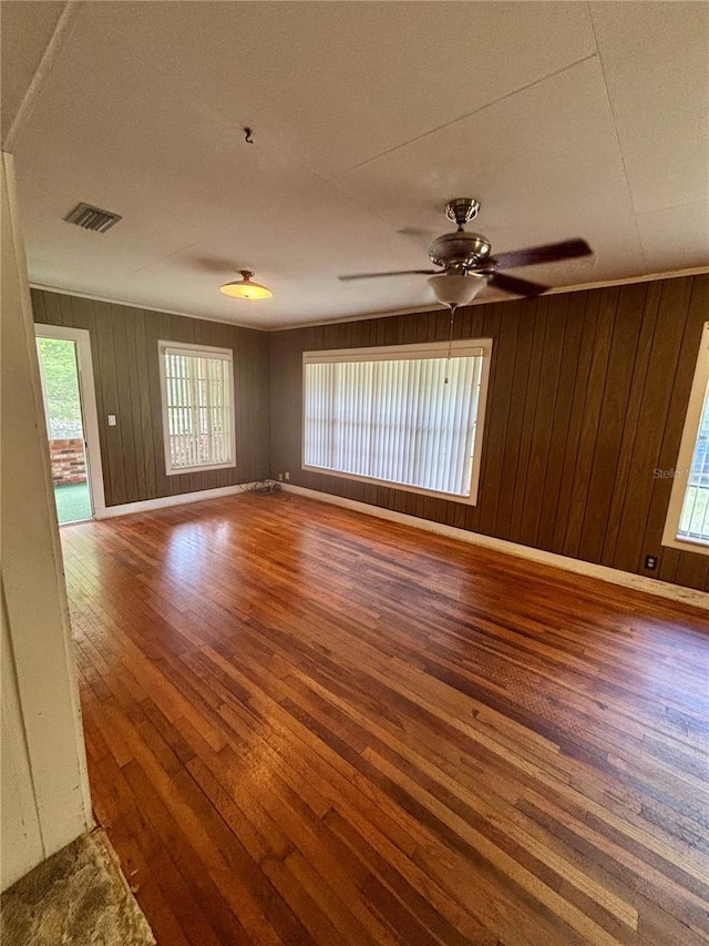 unfurnished room with hardwood / wood-style flooring, baseboards, wood walls, and a ceiling fan