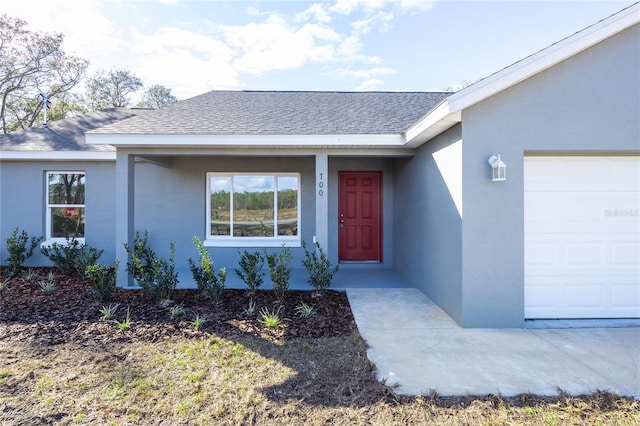 view of exterior entry featuring an attached garage, stucco siding, and a shingled roof